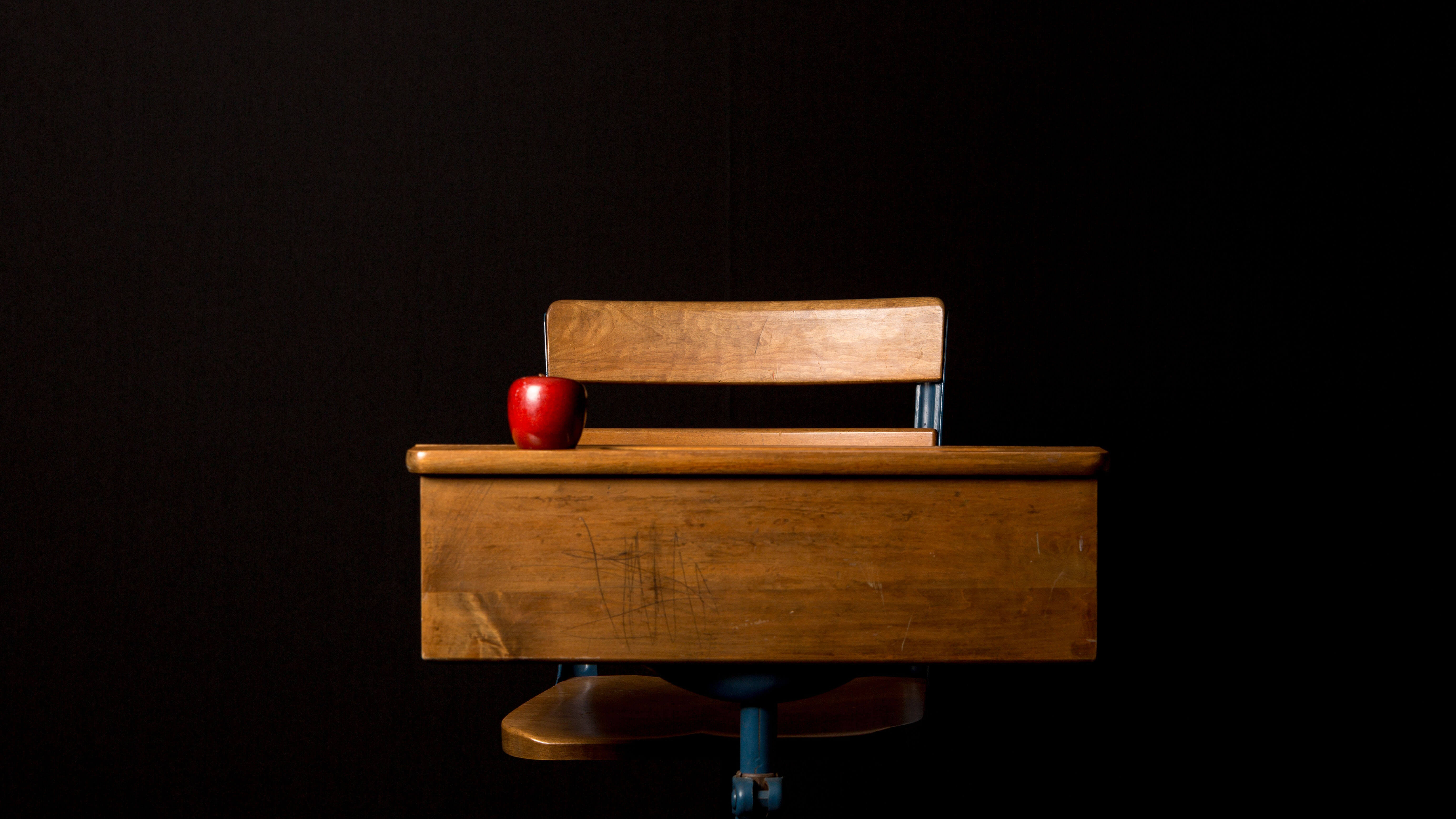 Mesa de estudante com maçã vermelha em cima e fundo preto atrás