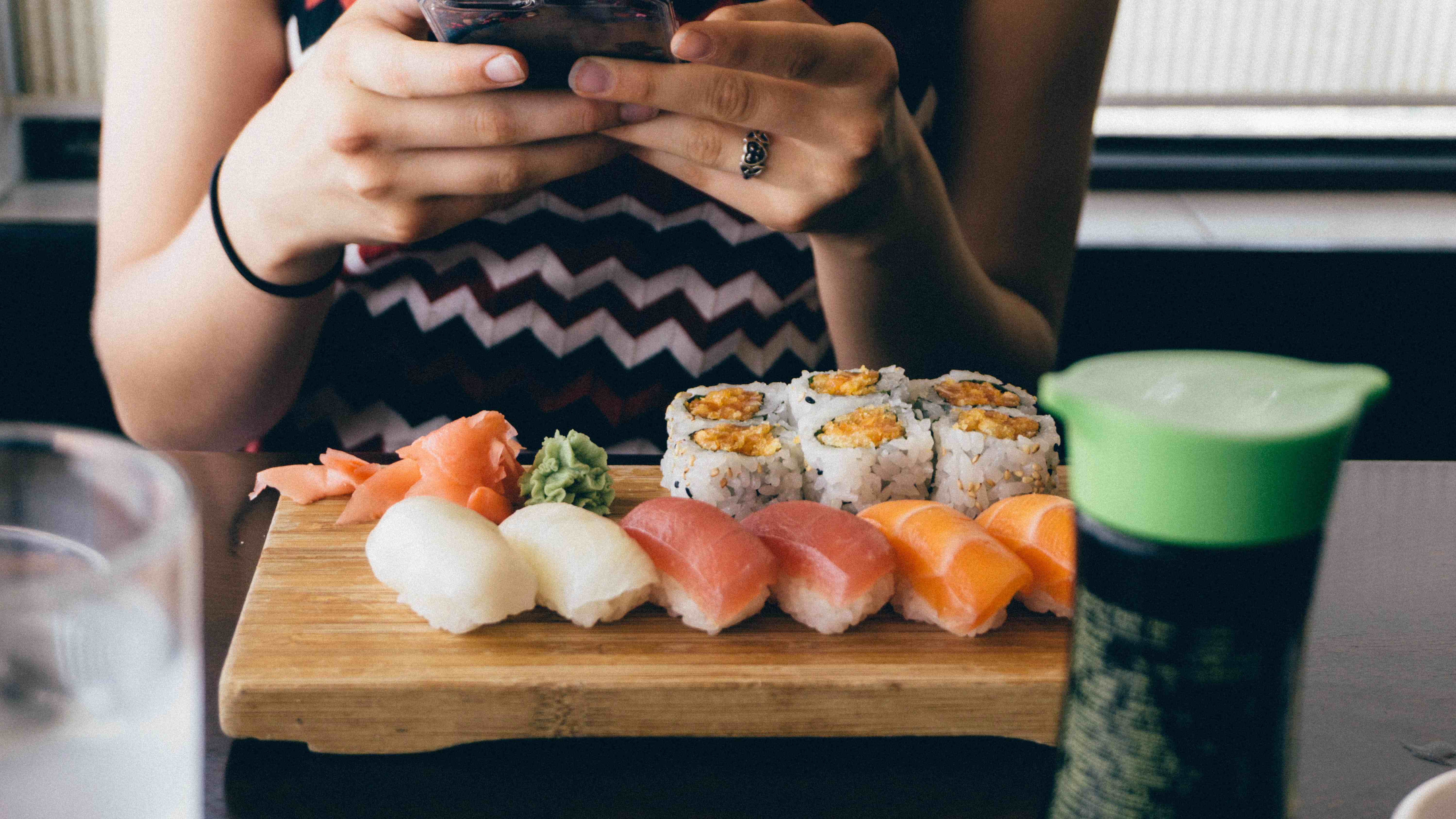 Mulher mexendo no celular com prato de comida japonesa na frente