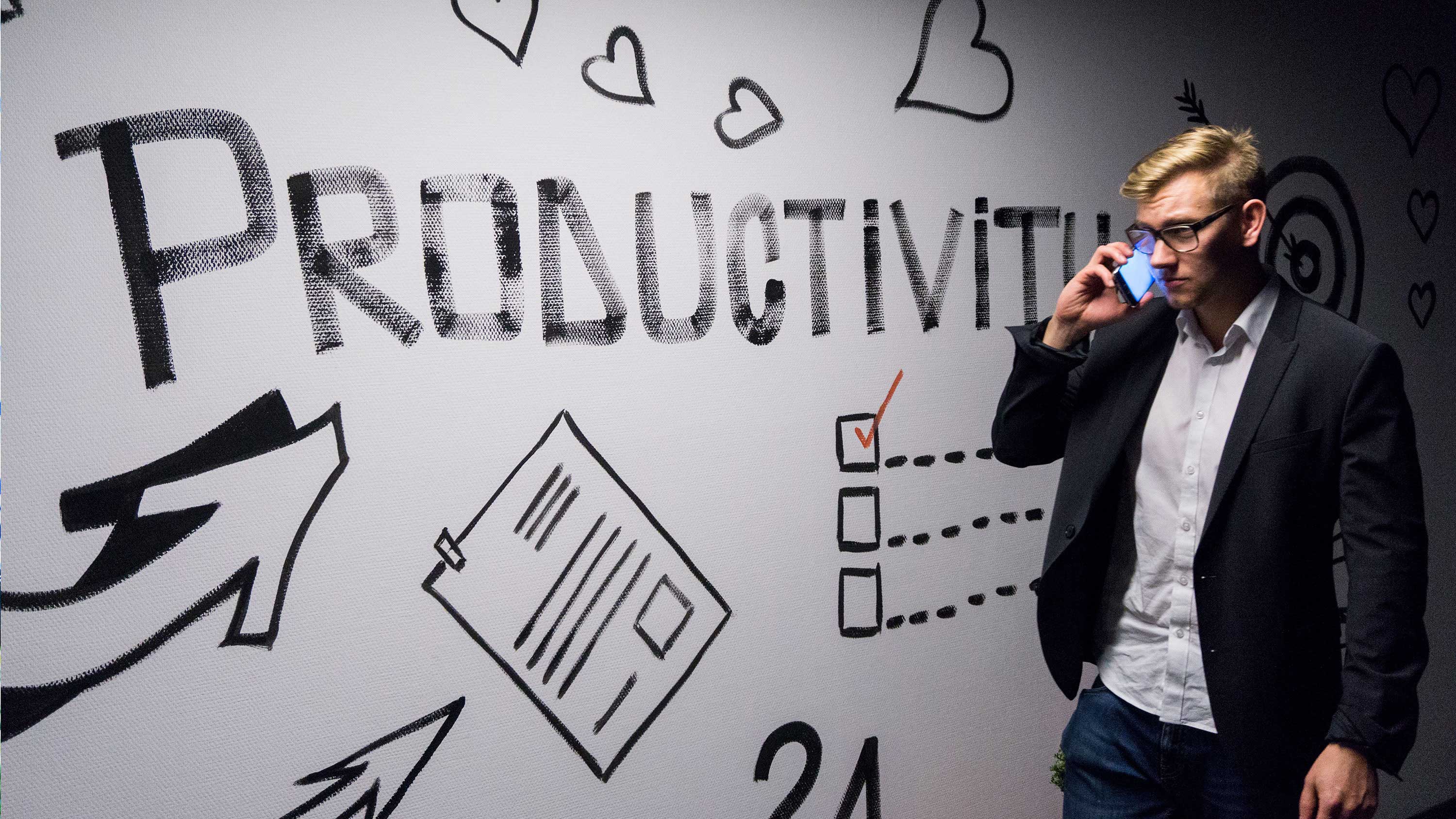 Homem falando ao celular diante de parede escrito "Produtividade".